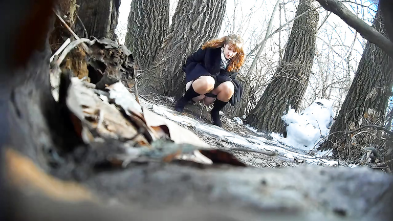 Ginger bridesmaid makes water behind a tree in the forest