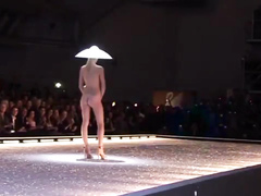 Seductive fashion model in a weird hat walks down the catwalk in the nude