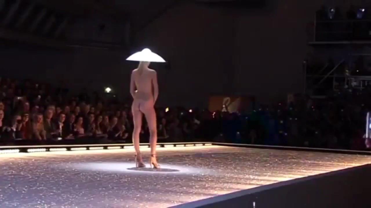 Seductive fashion model in a weird hat walks down the catwalk in the nude voyeurstyle