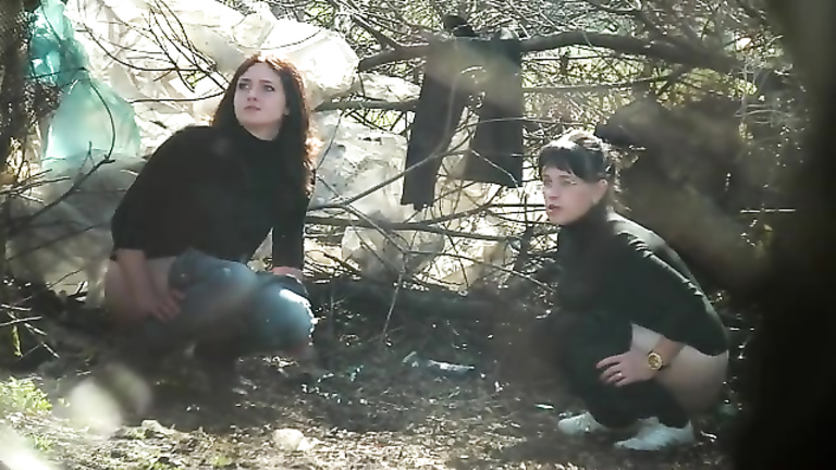 Women in turtlenecks and jeans relieve themselves in the woods